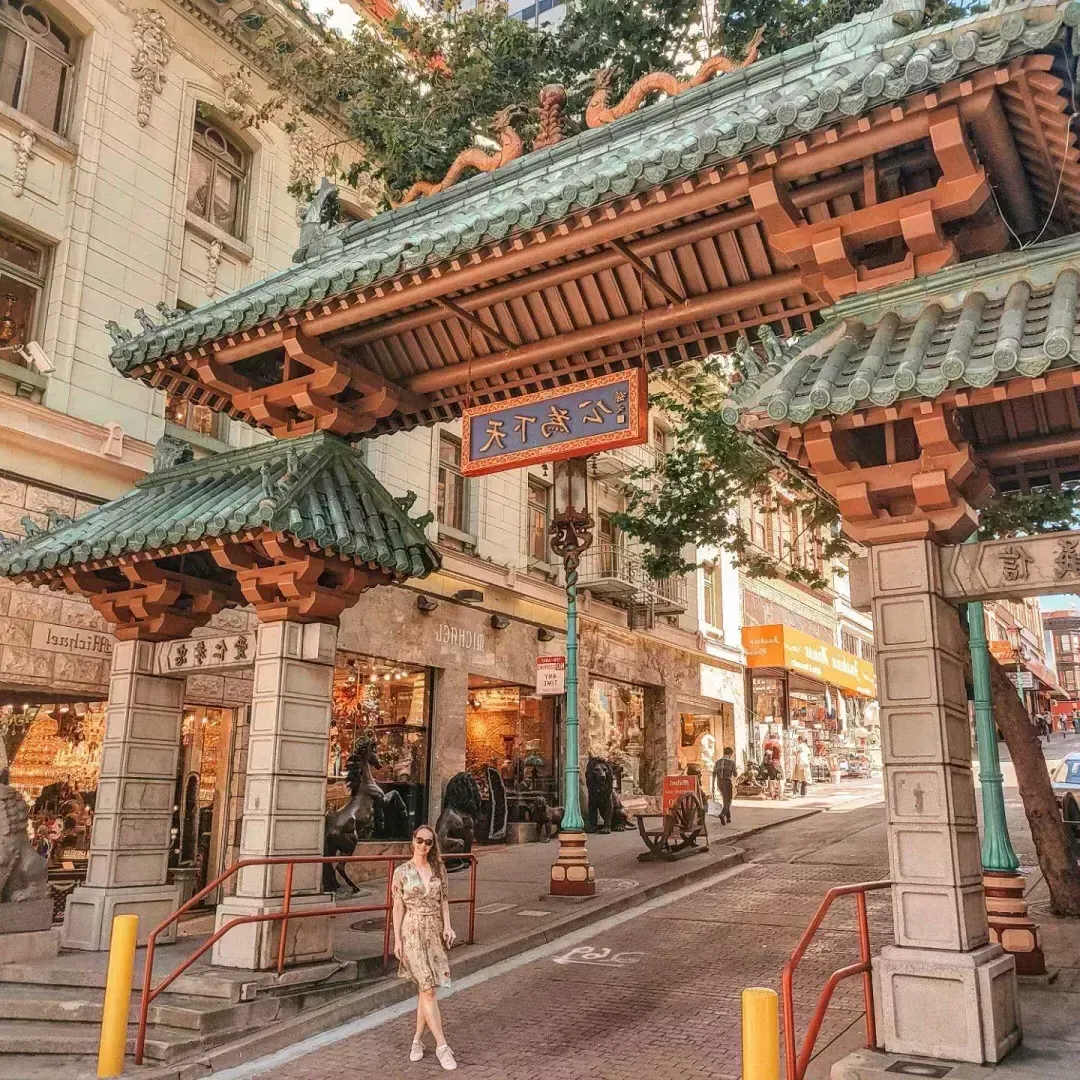 Uma mulher posa em frente a um portão ornamentado que marca a entrada da Chinatown de São Francisco.